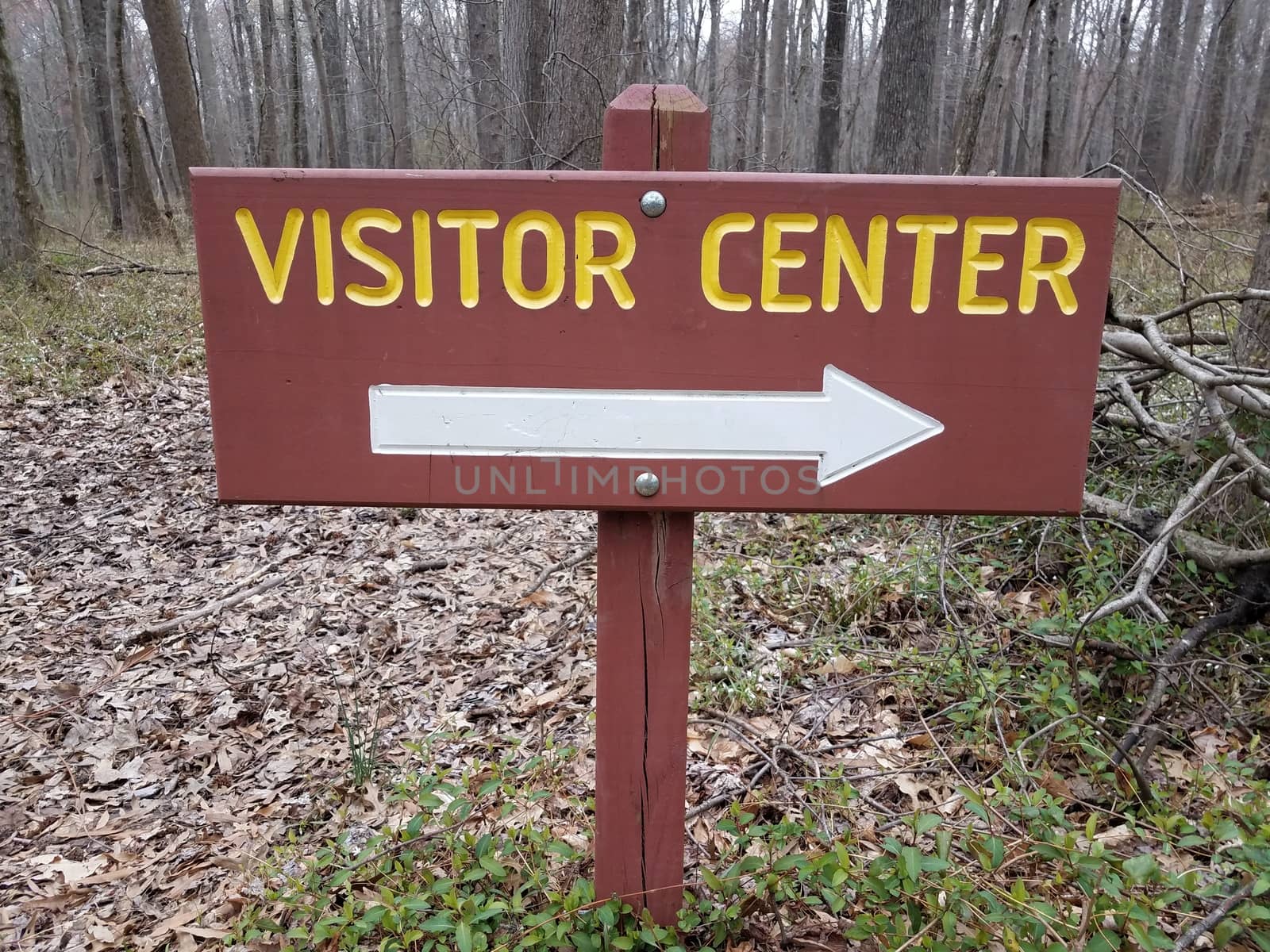 brown or red visitor center sign with white right arrow and trees in the forest or woods