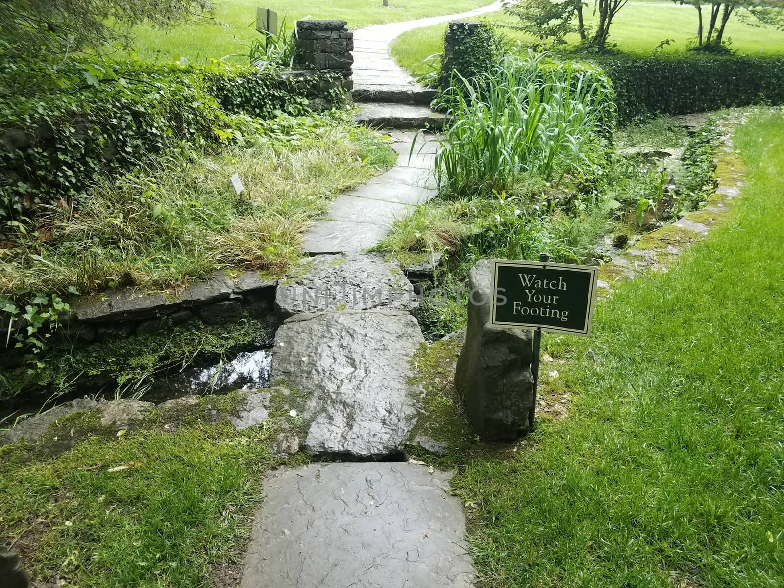 watch your footing sign and stone path and tiles and bridge over water by stockphotofan1