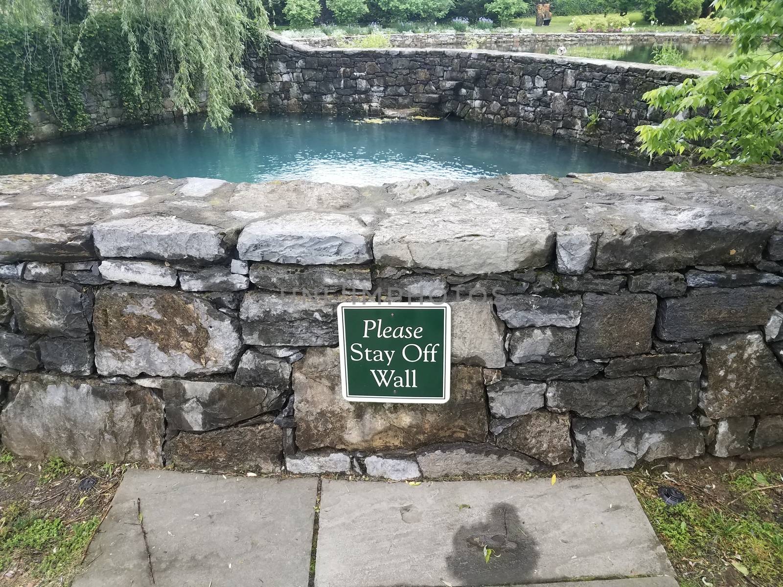 please stay off wall sign on stone wall with water or pond