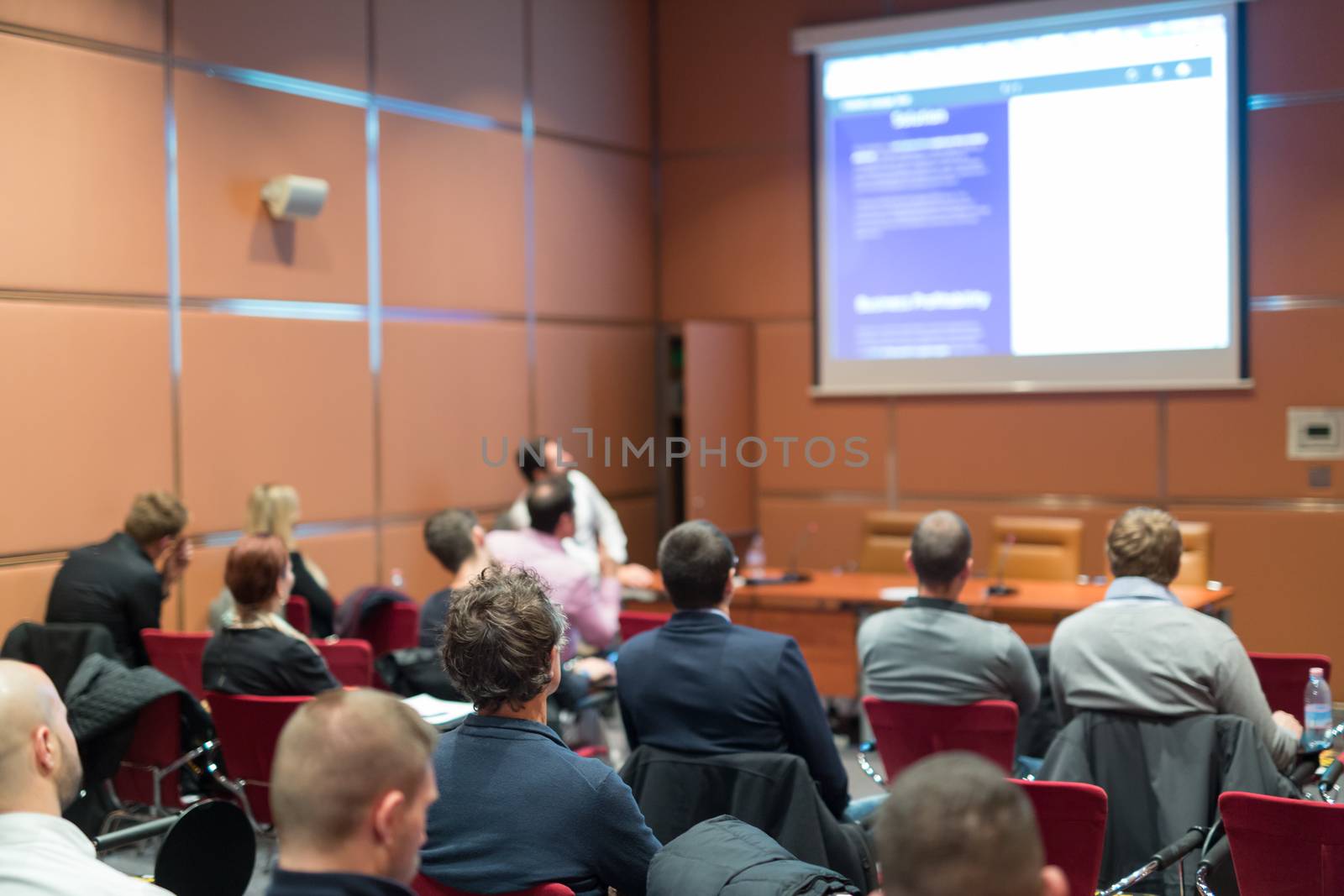 Public Speaker Giving a Talk at Business Meeting. Audience in the conference hall. Focus on unrecognizable man in audience. Business and Entrepreneurship concept.