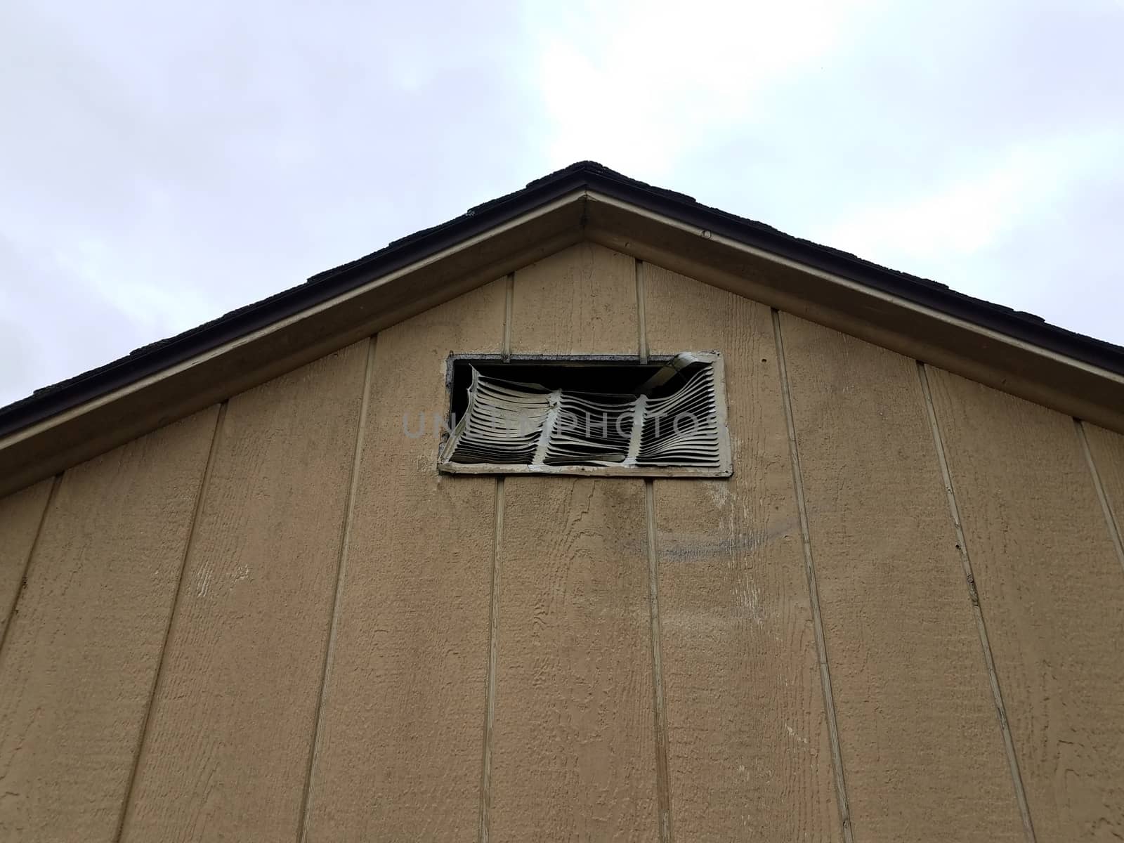 brown storage shed building with damaged or broken metal vent