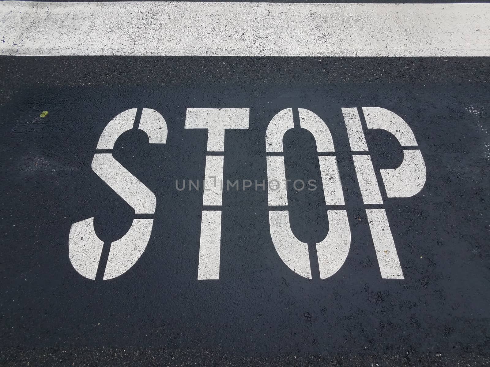 white stop sign painted on black asphalt street or road