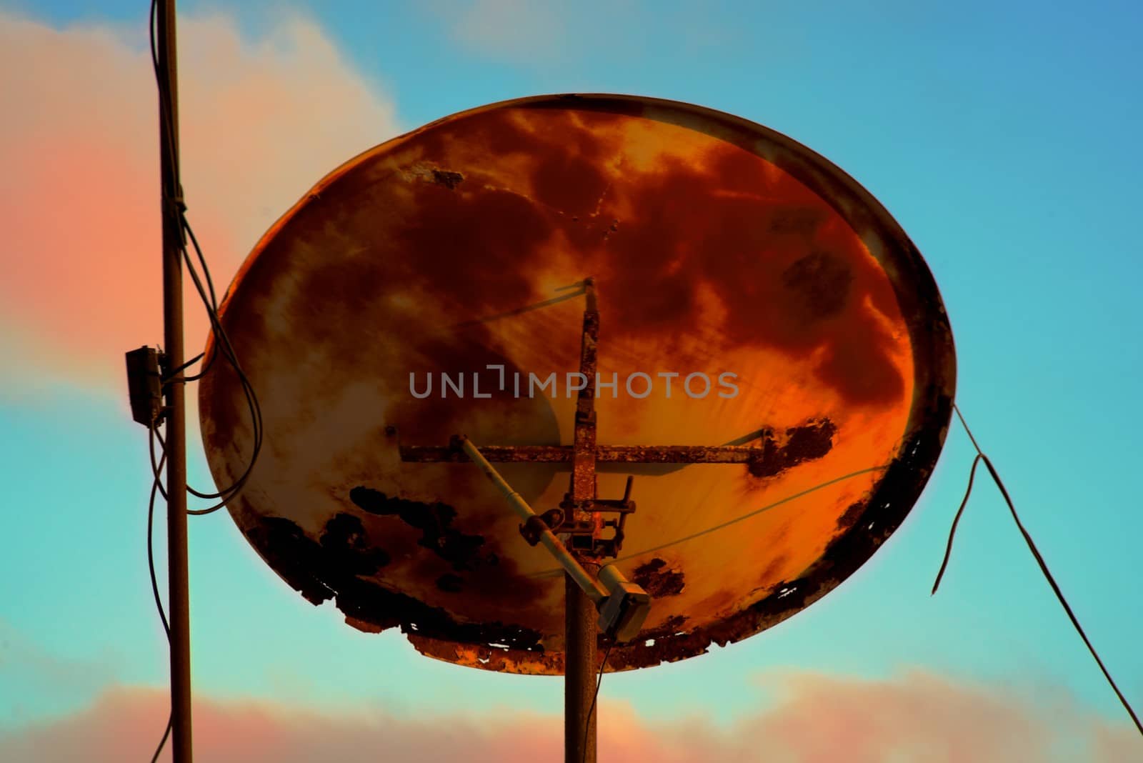 back of a very old rusty satellite television antenna with cloudy sky background at sunset
