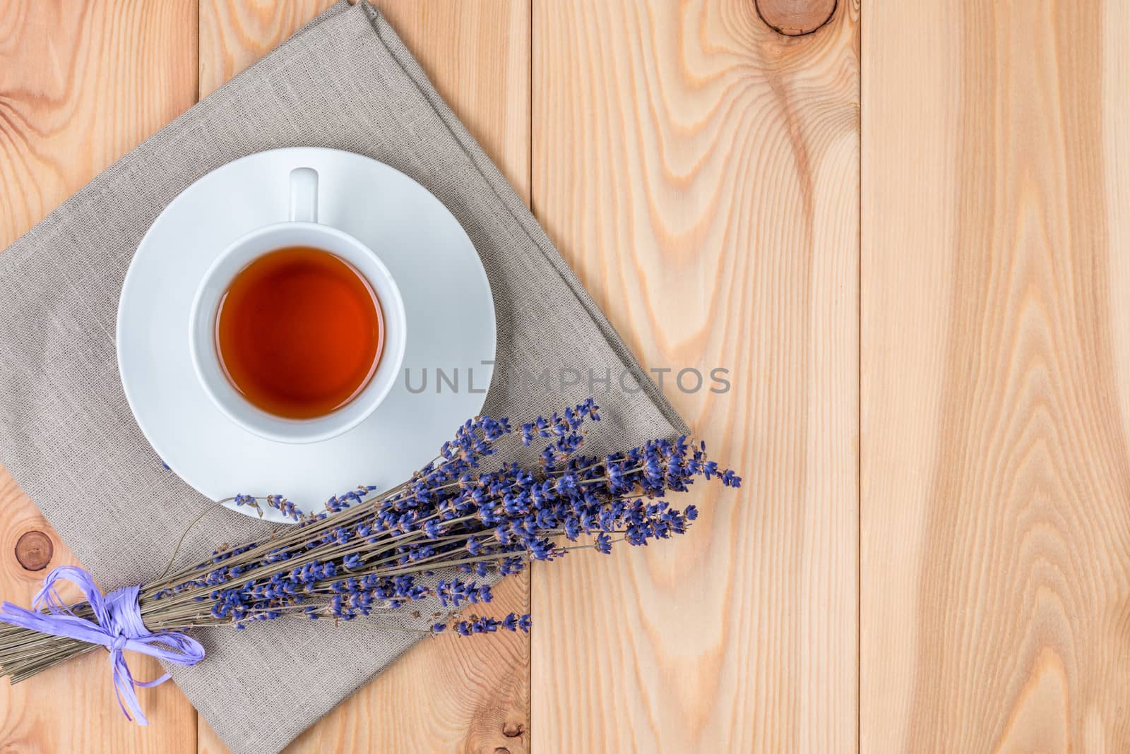 a cup of soothing tea with lavender and a bunch of flowers on a linen napkin on wooden planks; top view; on the right is space for an inscription