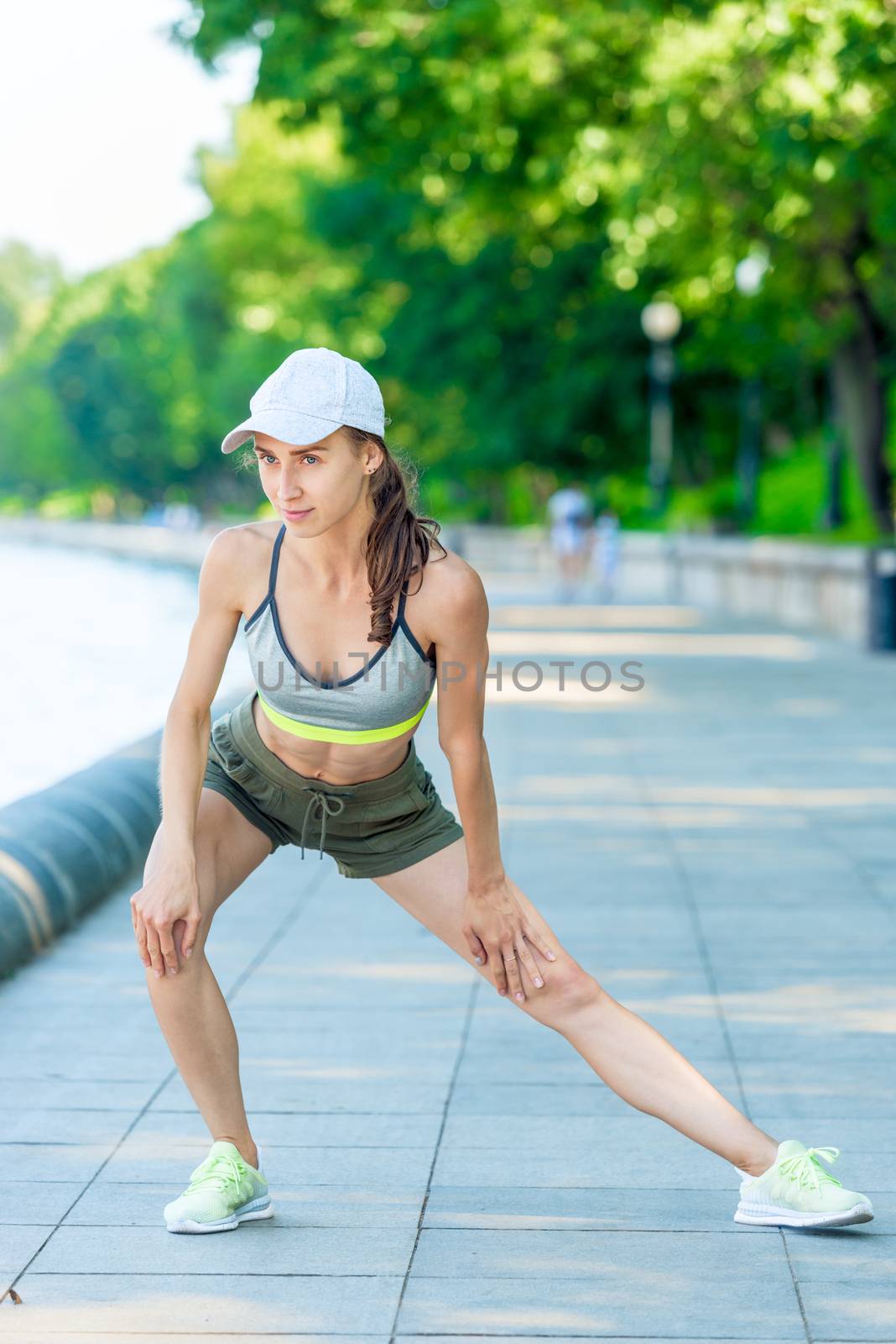 woman in sportswear with a muscular figure is warming up on the city embankment before jogging