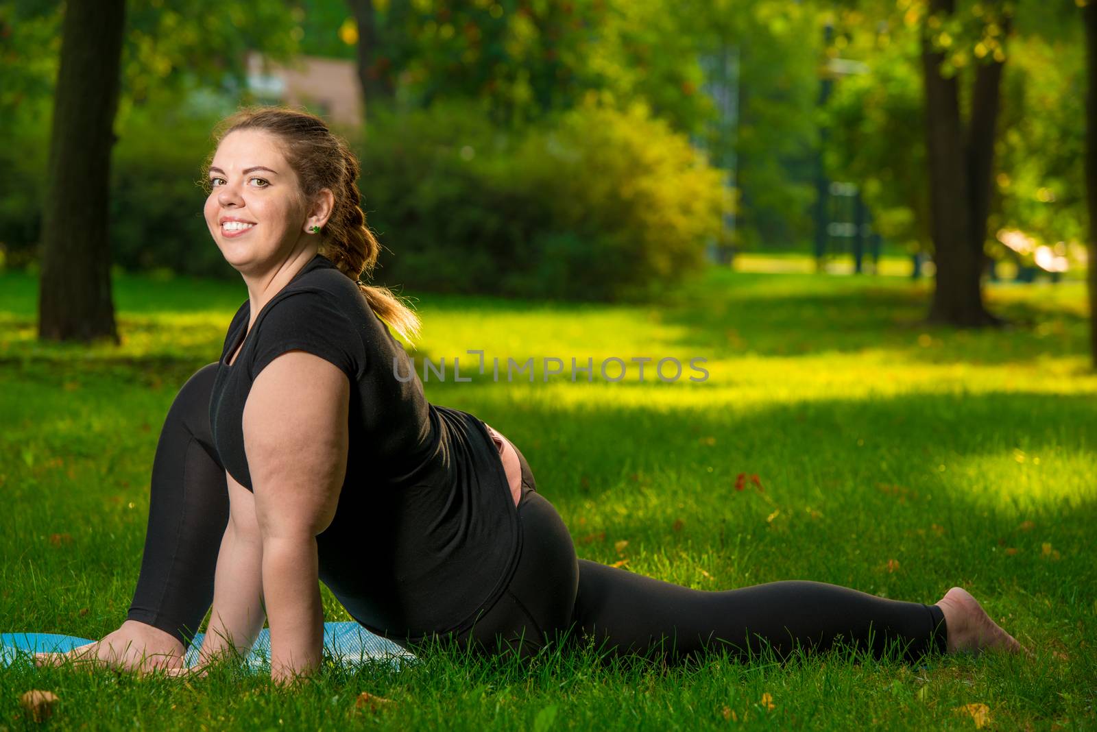 young flexible and beautiful woman plus size in the park on the lawn performs stretching exercises