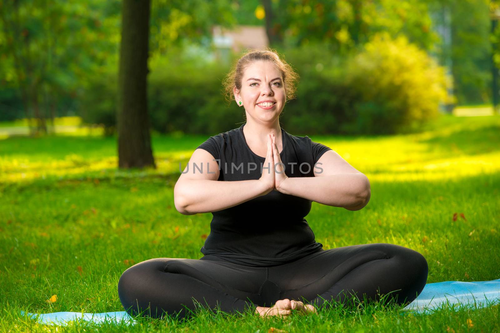 plus size woman posing in park performing exercises in lotus pose