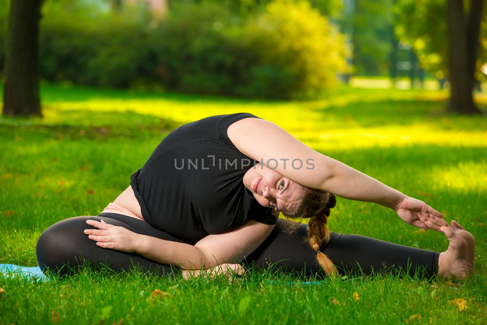 flexible plus size woman doing yoga in the park on the lawn by kosmsos111