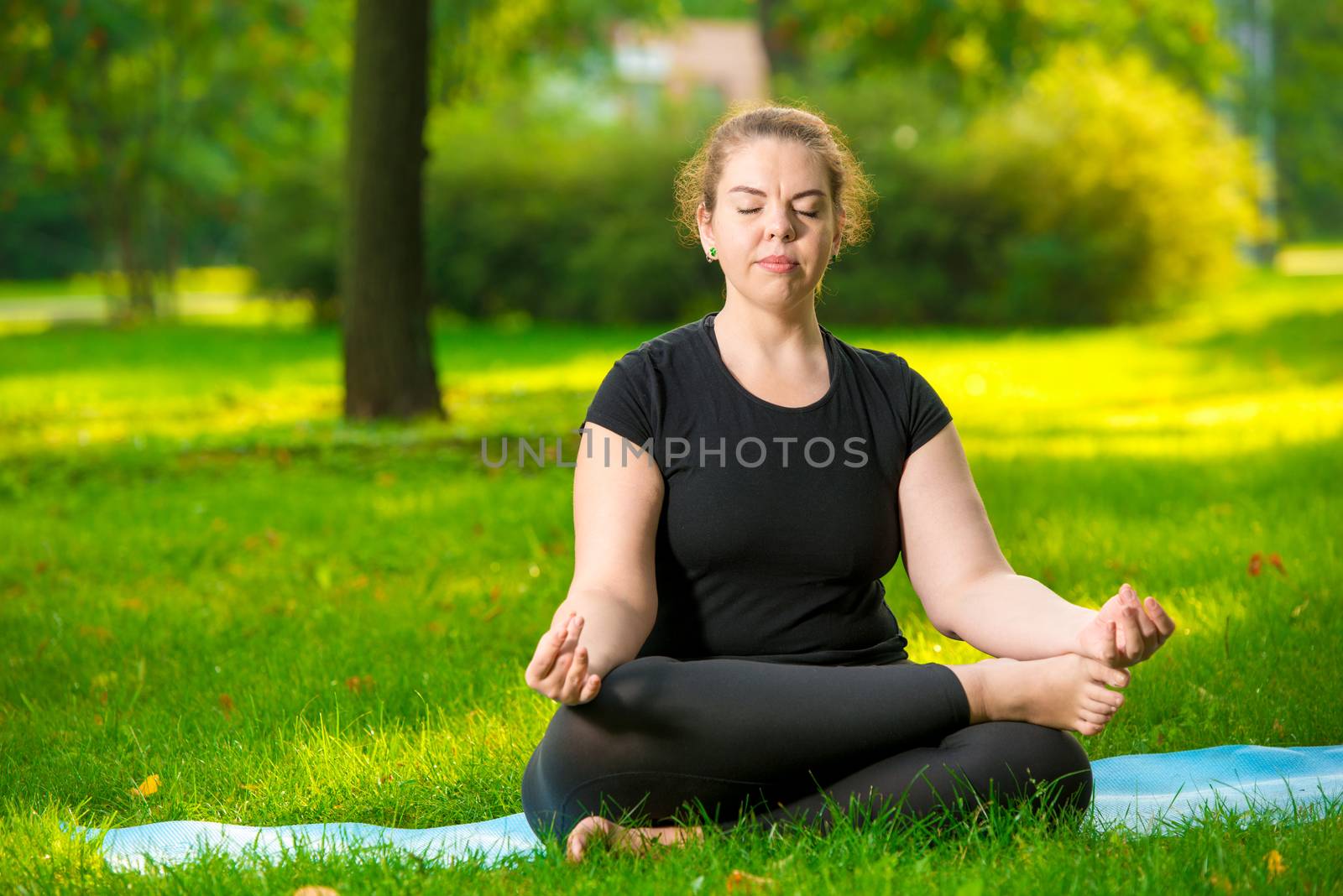concentrated woman oversize meditates on the lawn in the park in the lotus position