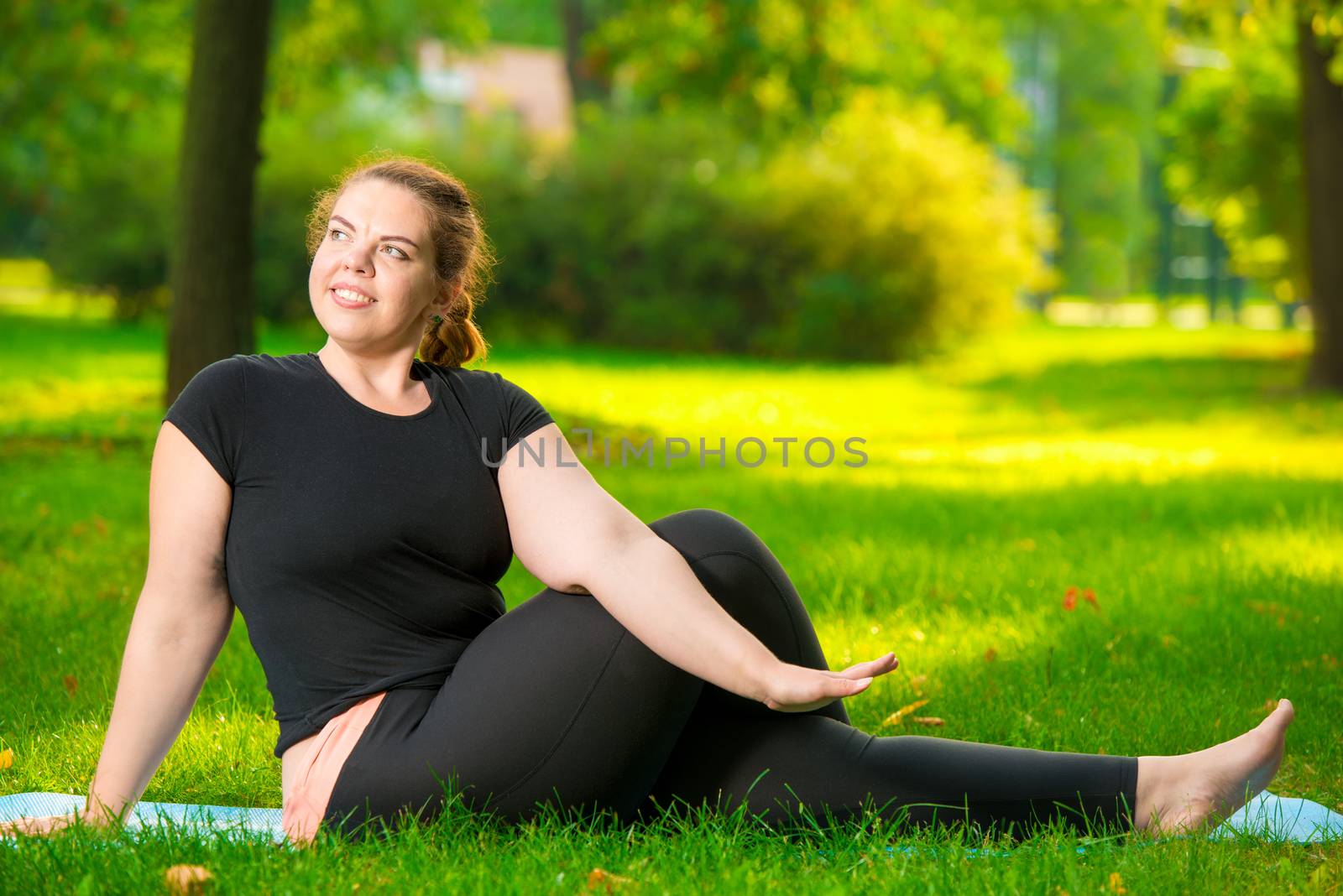 happy over sized woman in the park doing yoga early in the morning on the lawn