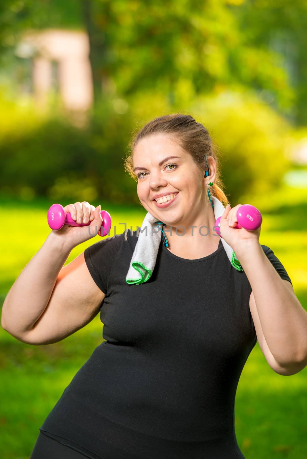 oversize woman in headphones with dumbbells in hand playing sports in park