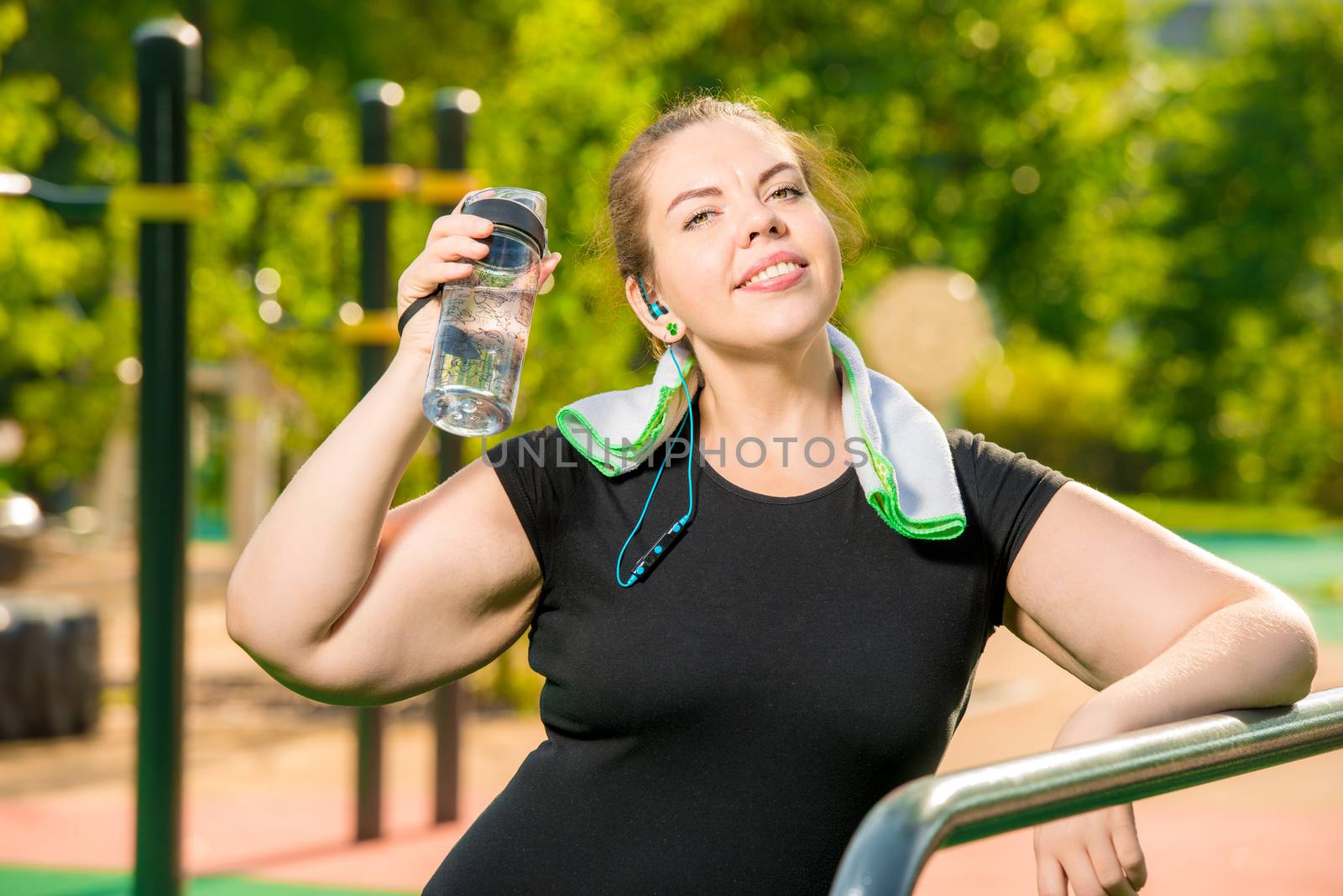 rest after training, portrait of a large woman with a bottle of water next to the simulator in the park