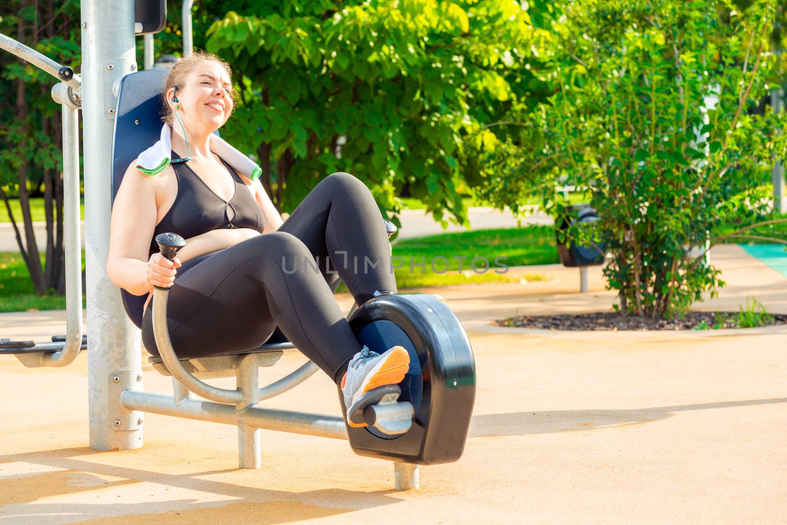 happy and active oversized woman doing exercise on a stationary bike in a city park