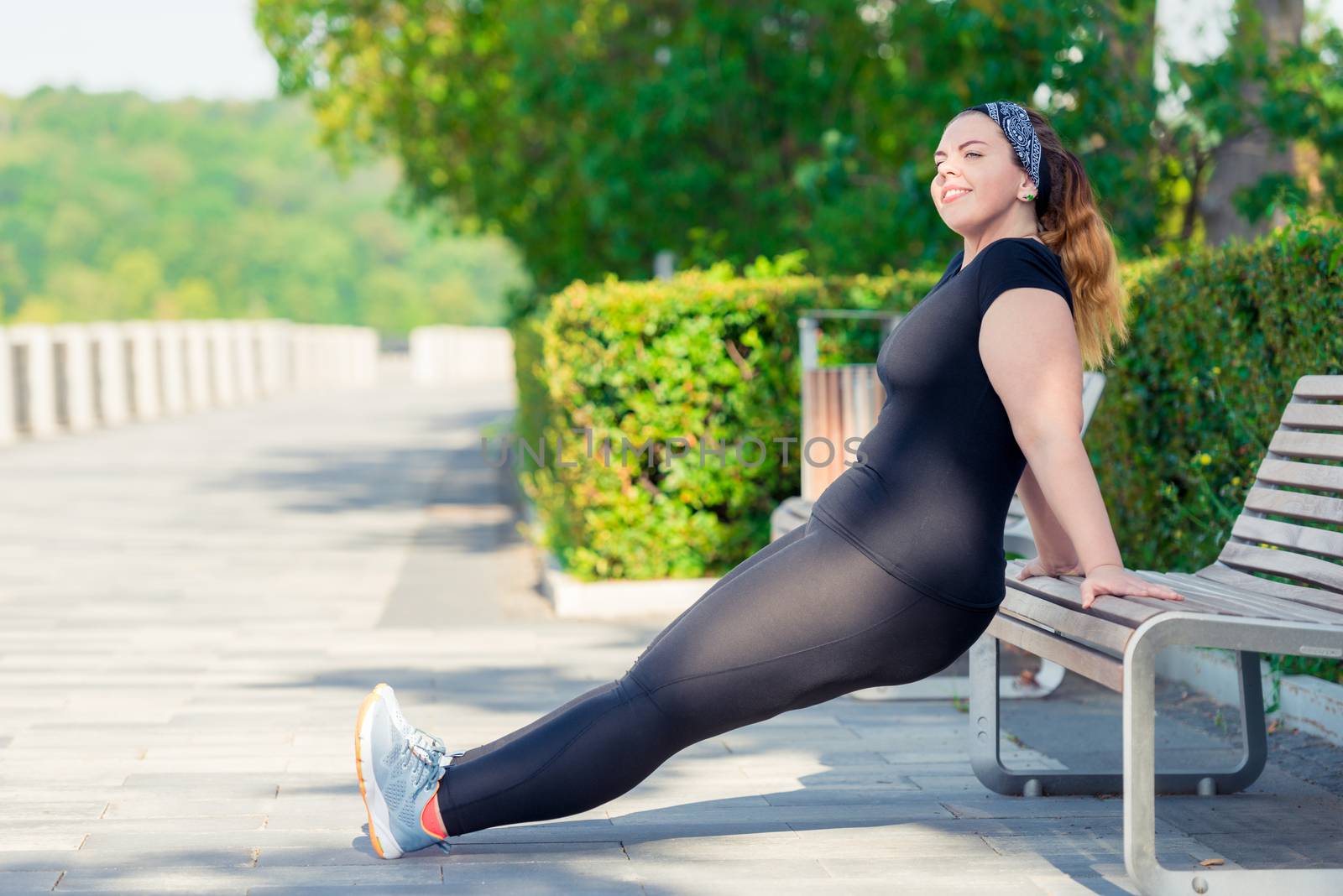 portrait of active happy plump woman performs exercises in the park on a bench