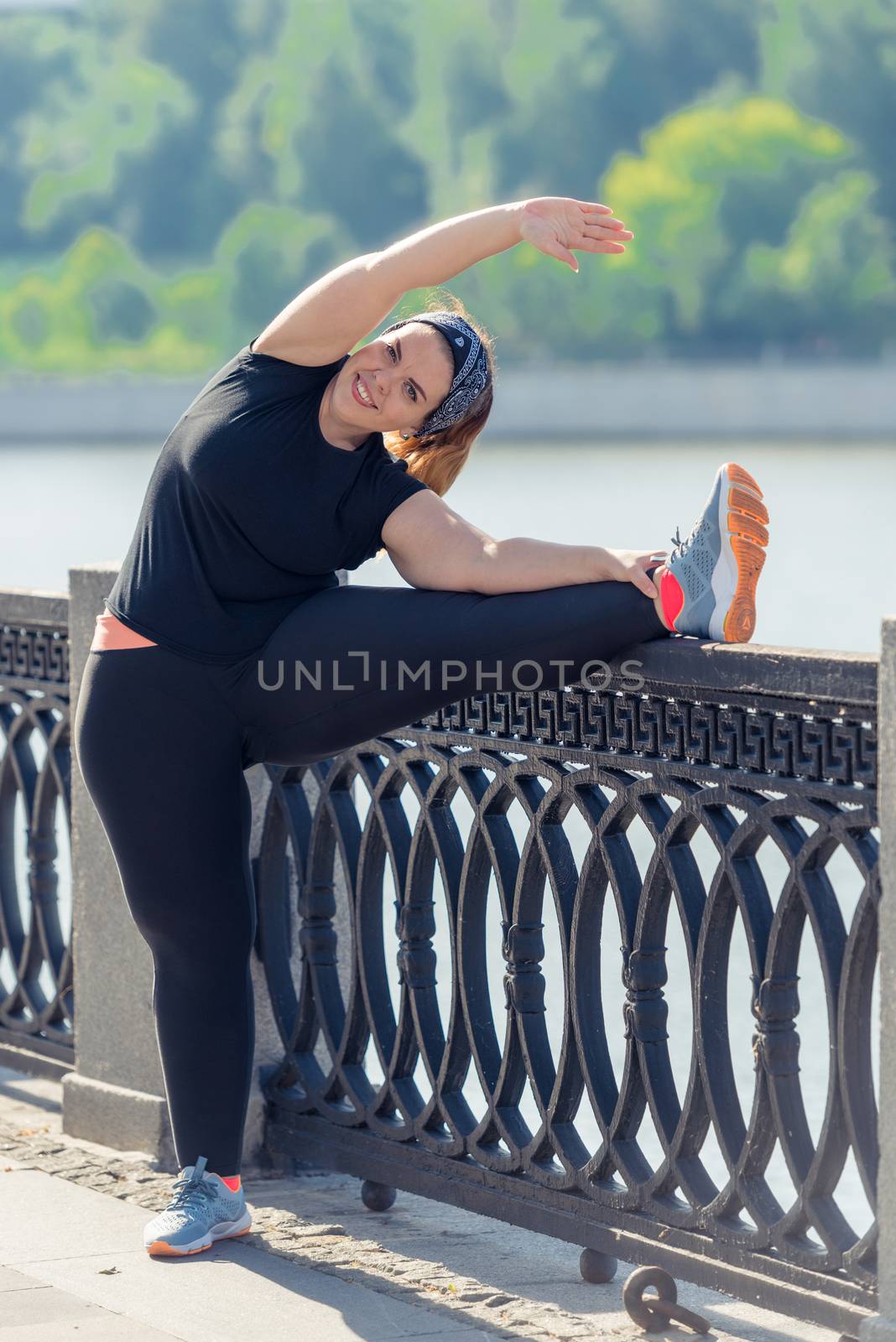 very flexible stout woman performs exercises on the embankment in the city park in the early morning