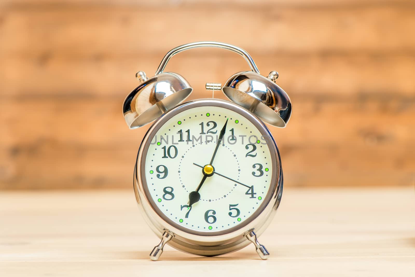 Silver alarm clock in retro style on a wooden background close-up shows 7 am