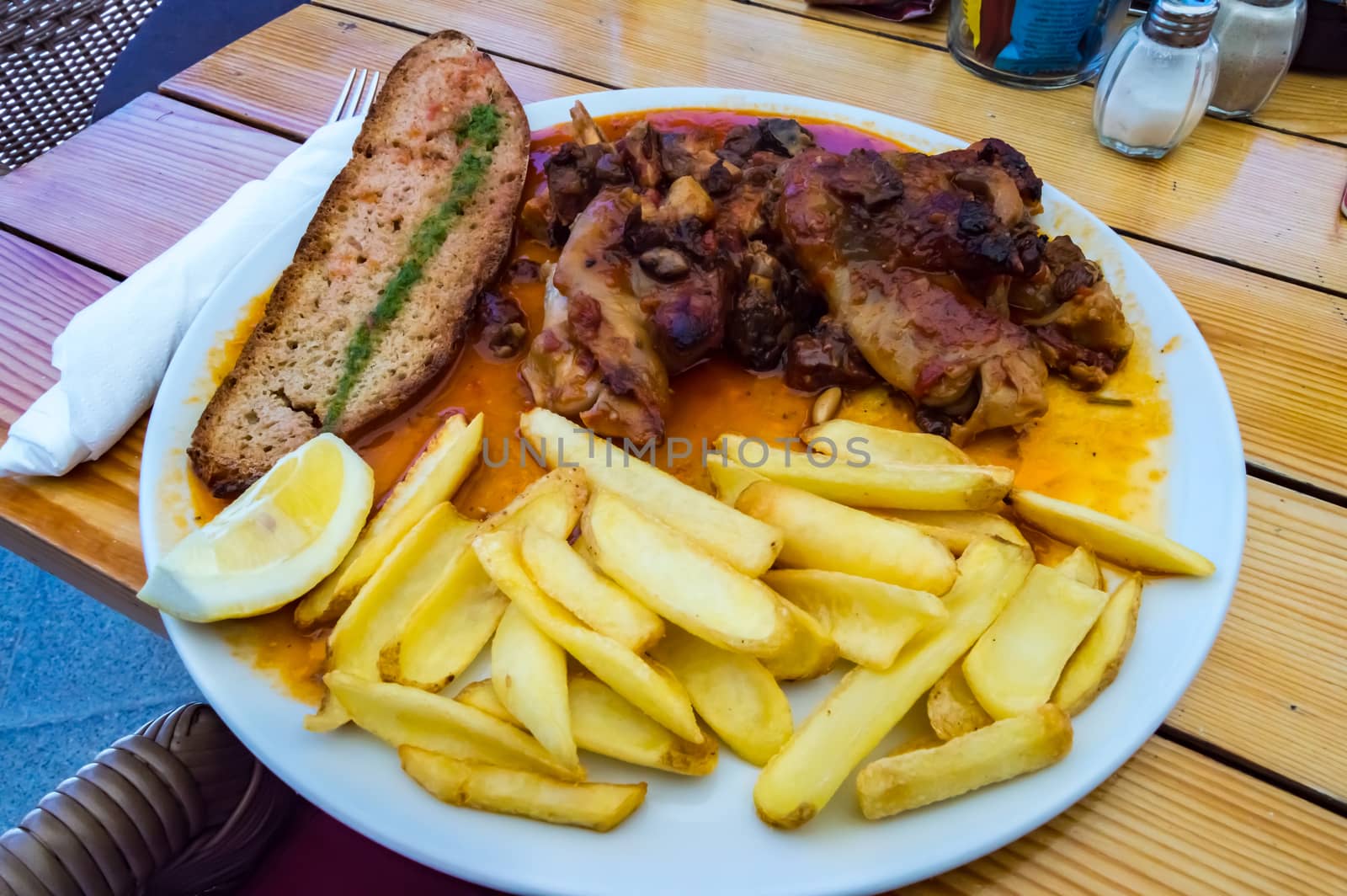 Plate of pig's feet with grapes with a slice of bread in the middle and fries of potato on a wooden table