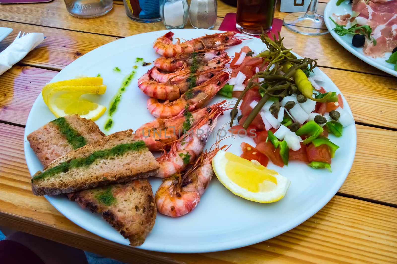 Plate of roasted prawns with slices of bread in the middle and tomatoes on a wooden table