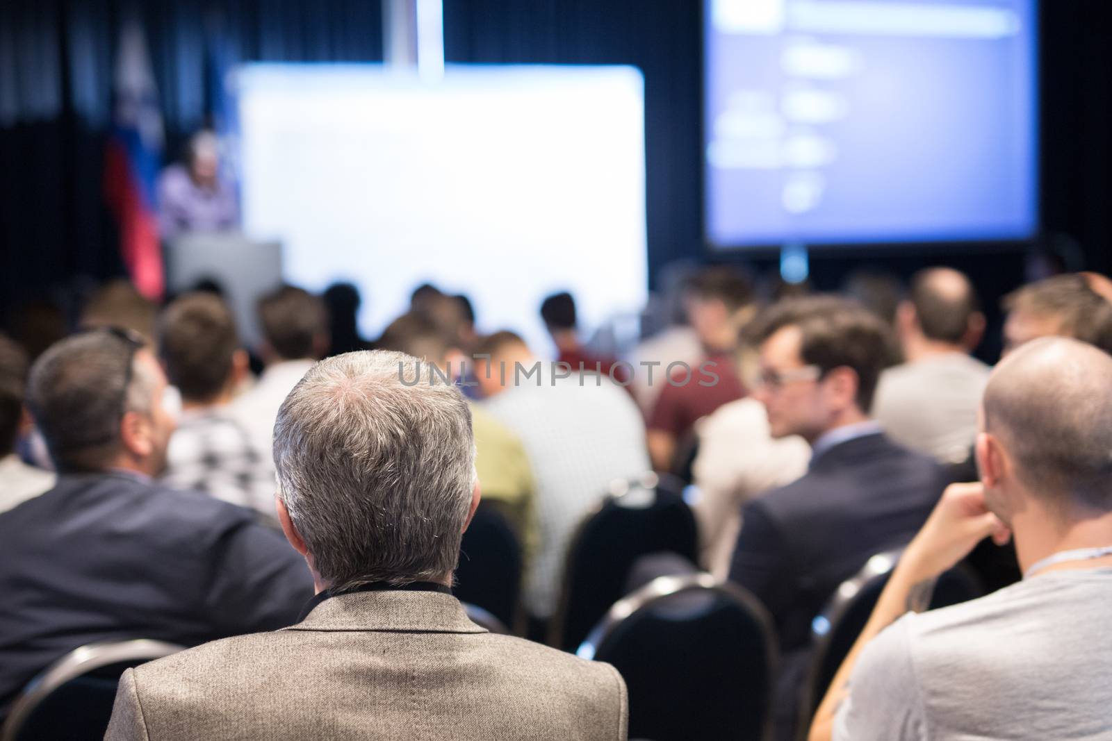 Speaker giving a talk in conference hall at business event. Audience at the conference hall. Business and Entrepreneurship concept. Focus on unrecognizable people in audience.