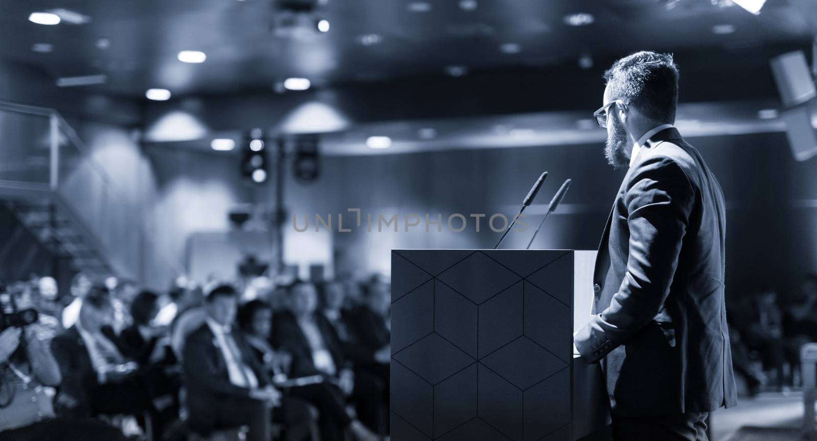 Businessman takes a picture of corporate business presentation at conference hall using smartphone. Business and Entrepreneurship concept. Focus on unrecognizable person in audience.