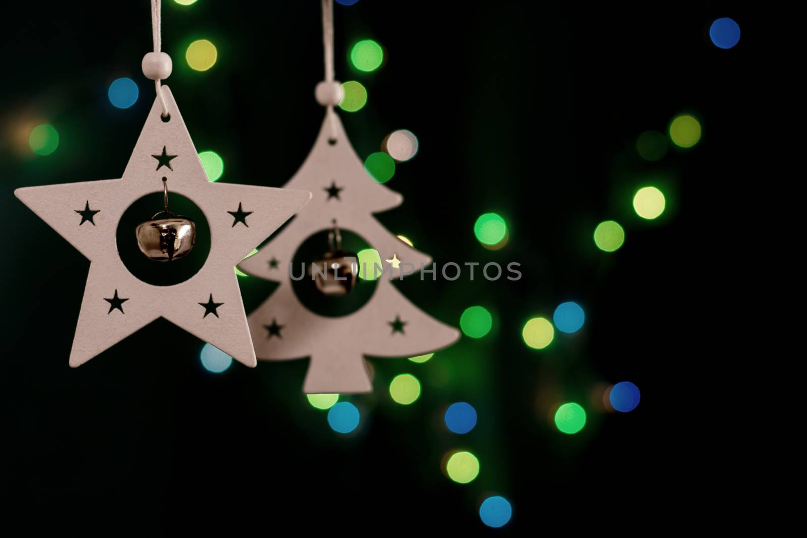 Handmade christmas decorations, star and fir tree with small round bells on dark background with colorful bokeh lights