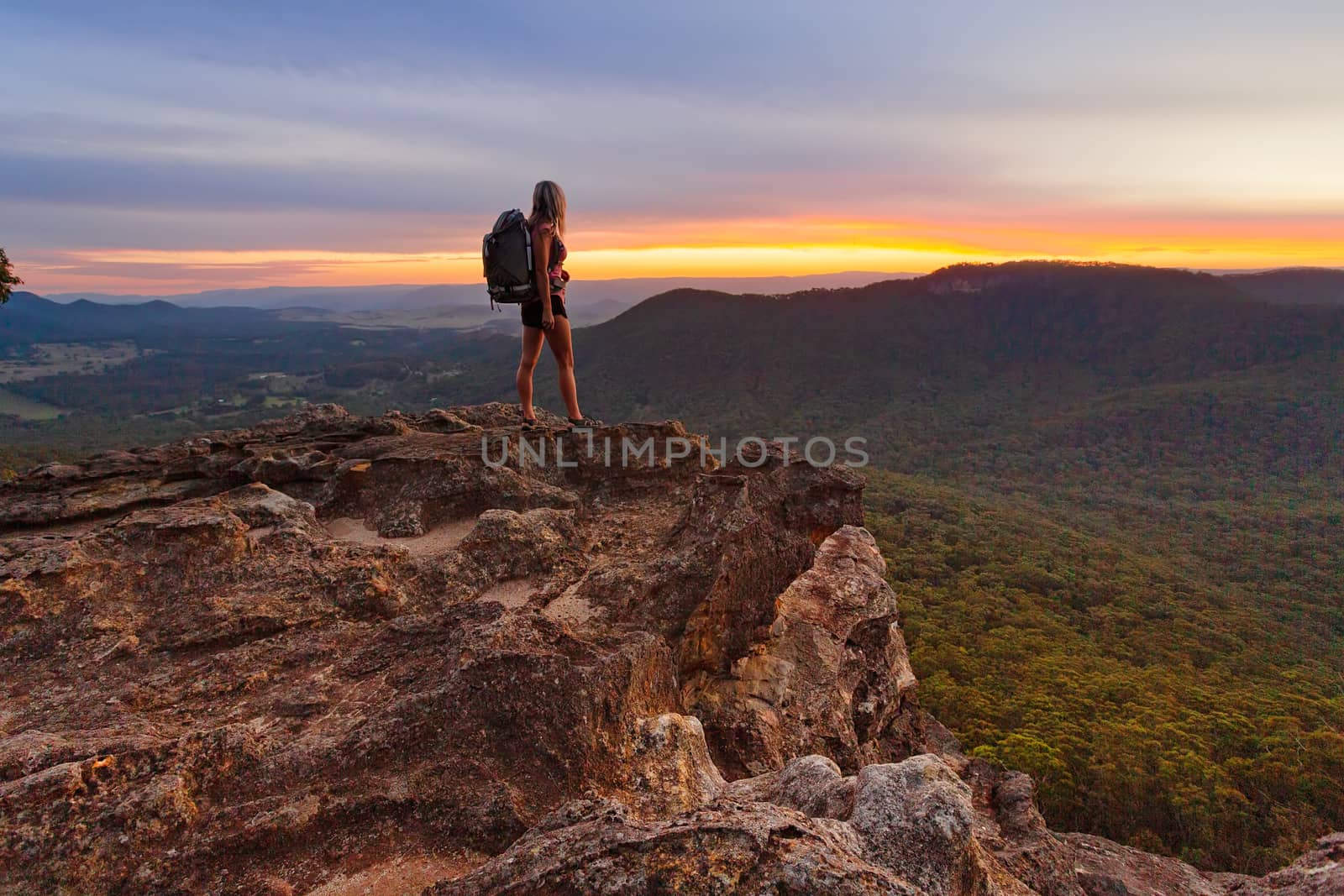 Hiker watching the last light  and fiery sunset colours fade as she watches lingering on with hope it will not end, but alas dusk and night will be swiftly upon her and the surrounding landscape of mountains and valleys