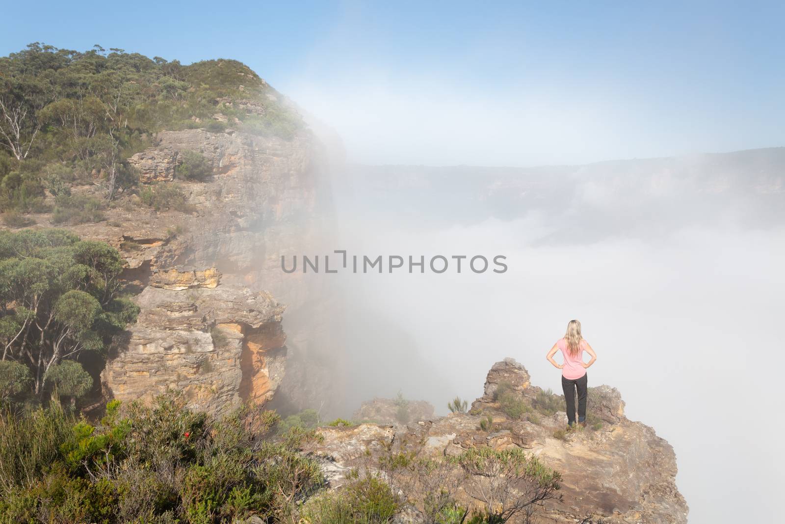 Female hiker standing on a rock pinnacle in Blue Mountains with rising fog and mist from the valley