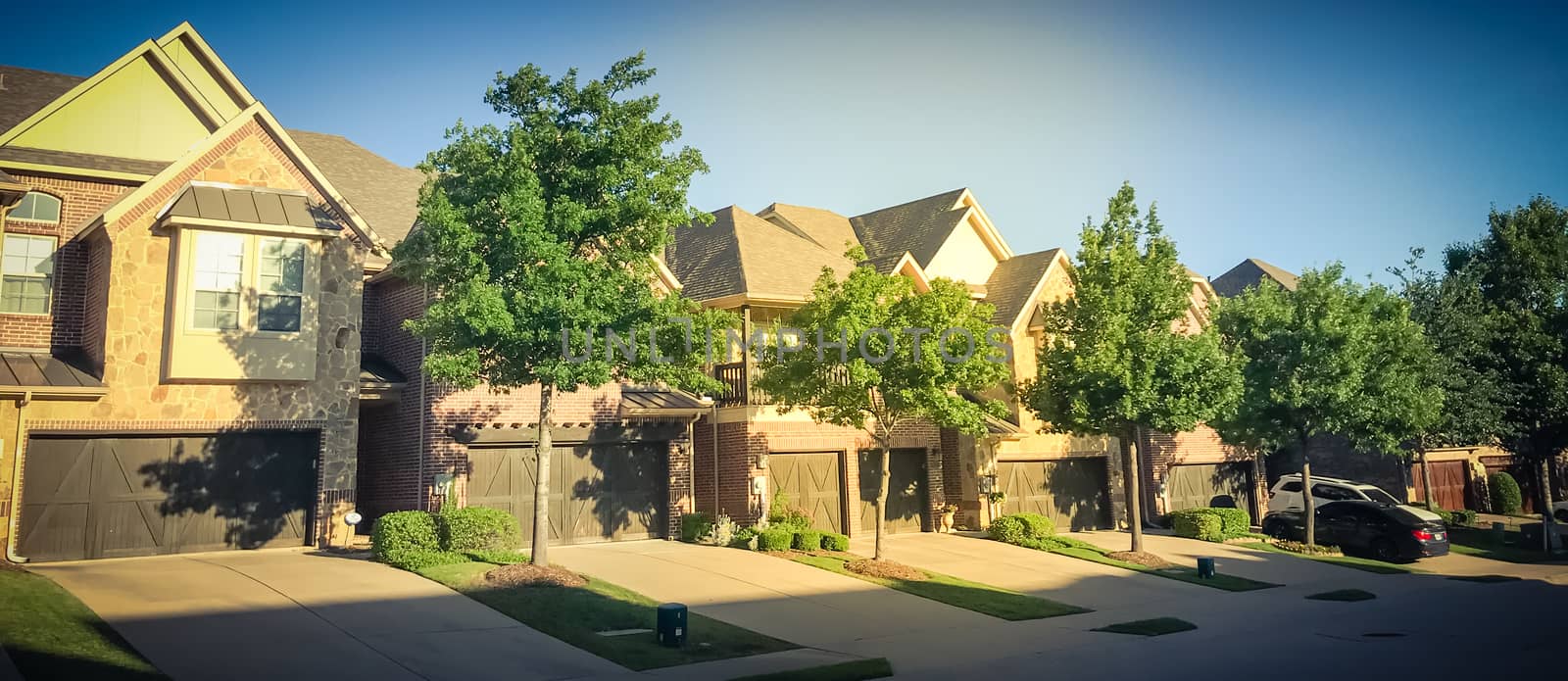 Panorama view row of brand new attached houses townhome style with double wooden garage doors and small front yard. Townhouse units outside Dallas, Texas, USA. Two stories house nice trim landscape