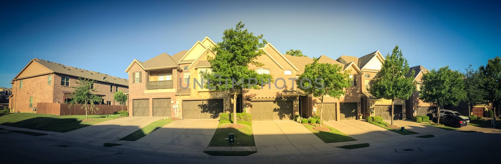 Panorama view row of brand new attached houses townhome style with double wooden garage doors and small front yard. Townhouse units outside Dallas, Texas, USA. Two stories house nice trim landscape