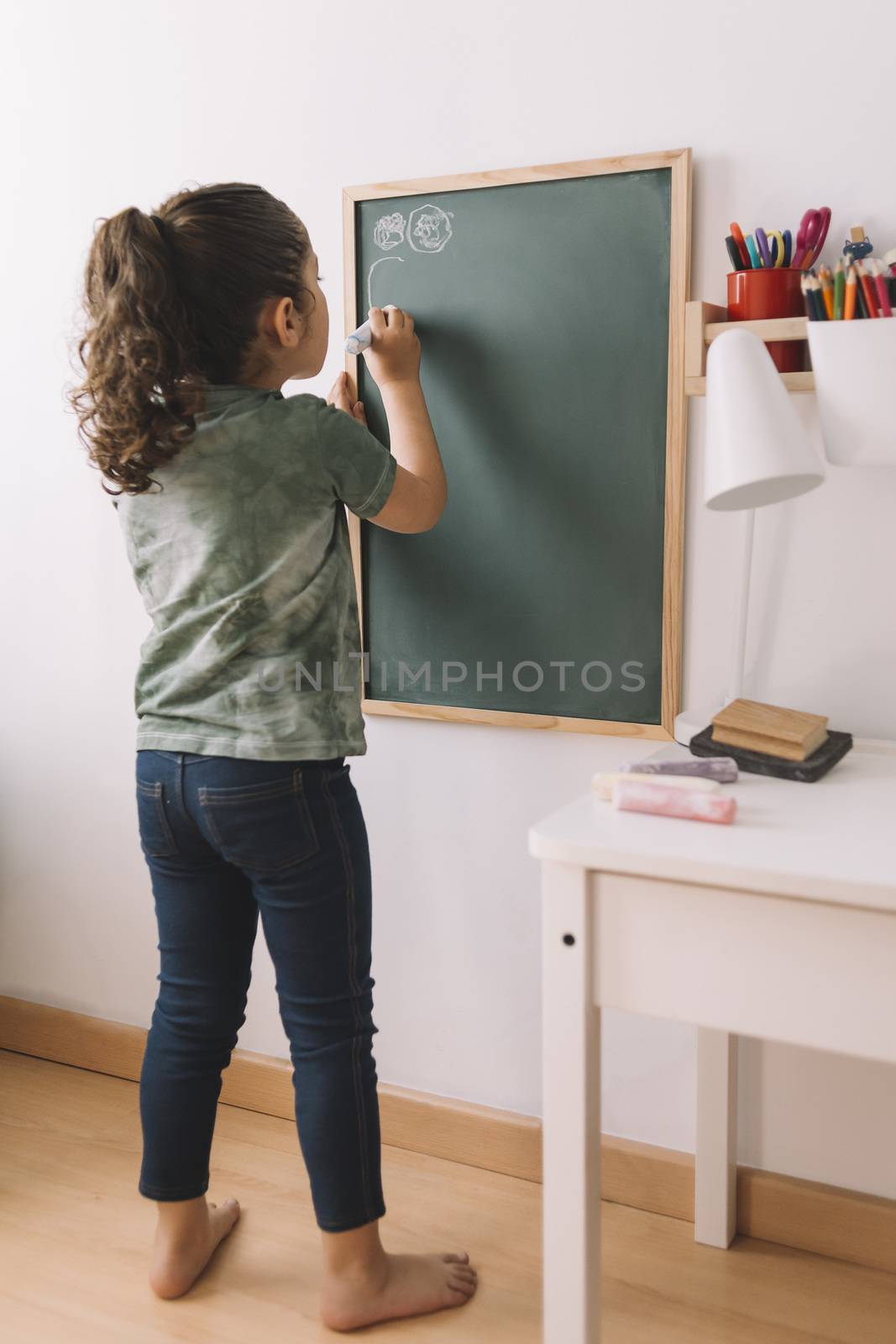 vertical photo of a little girl drawing with a chalk on the chalkboard at her room, copy space for text