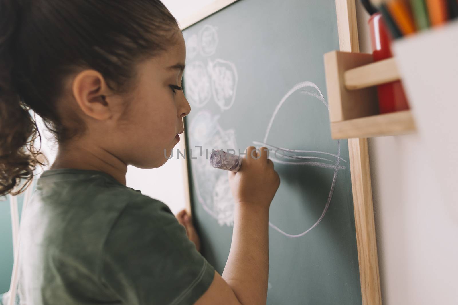 little girl drawing with a chalk on the chalkboard at her room at home, copy space for text