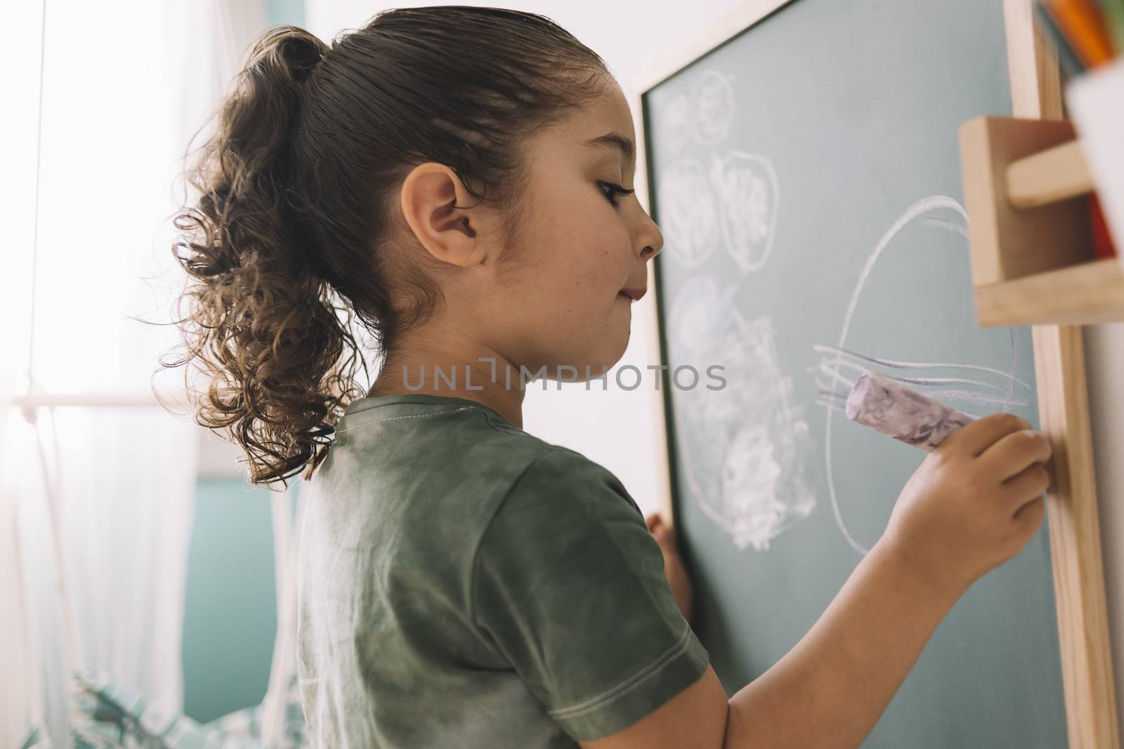 little girl drawing with a chalk on the blackboard at her room at home, copy space for text