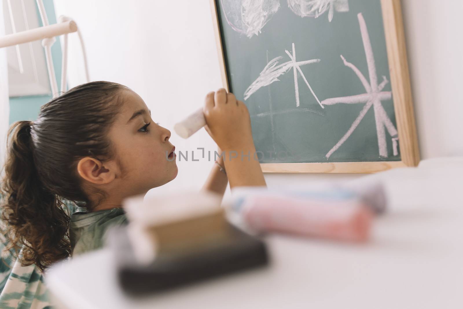 little girl concentrated drawing with a chalk on the blackboard at her room at home, copy space for text