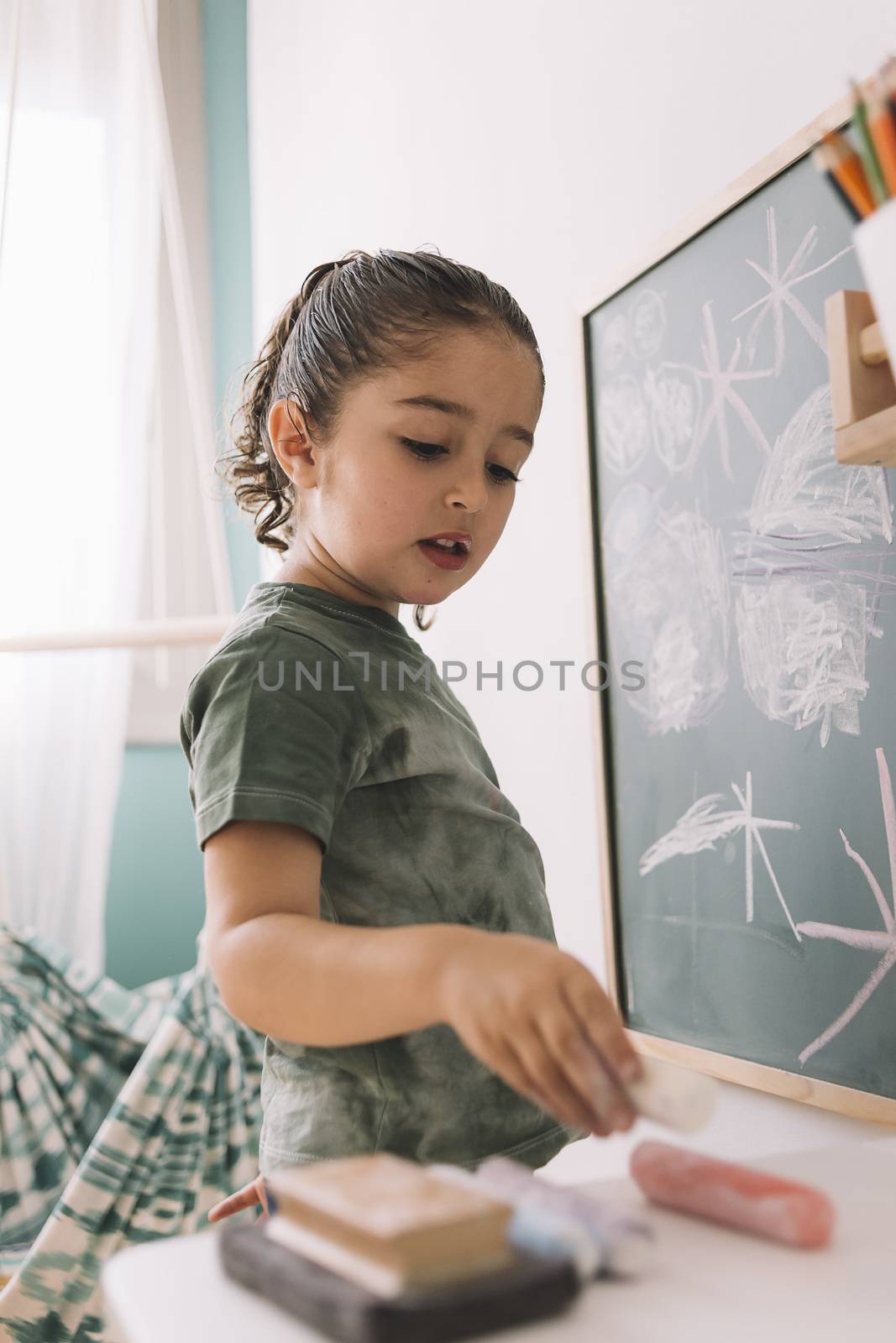 little girl picking up a chalk to draw on the blackboard at her room at home, copy space for text