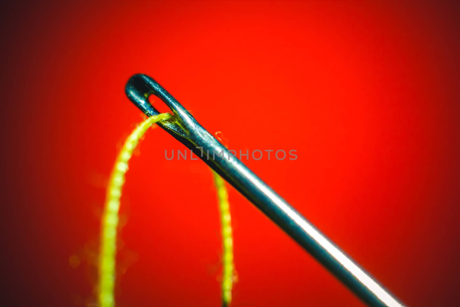 Needle and yellow thread through on orange background macro