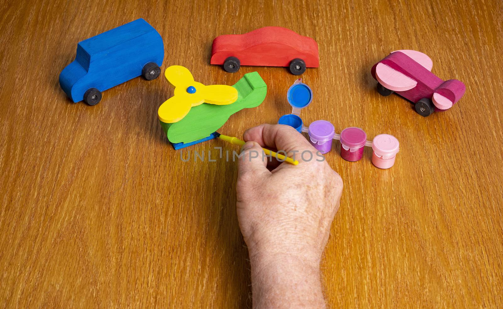 Painting the base of a wooden toy helicopter with other toy vehicles and paint in the scene.