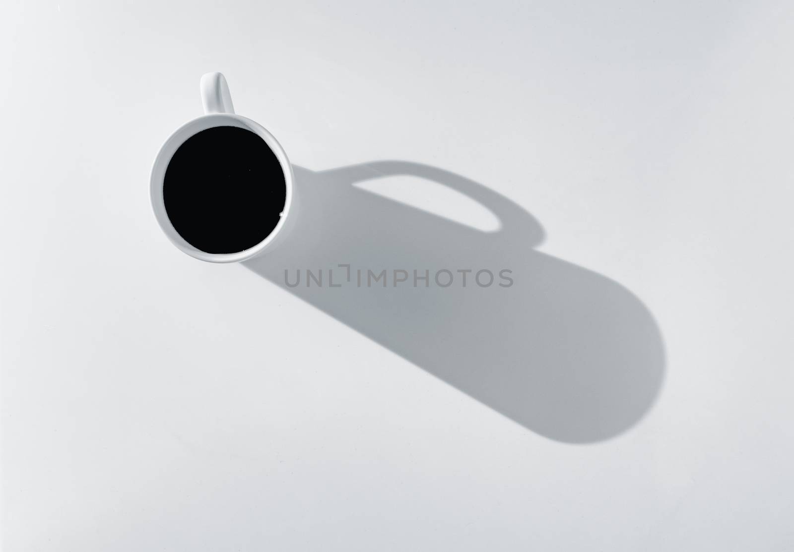 Coffee in cup on a white background, casting a strong shadow in this high key photo.