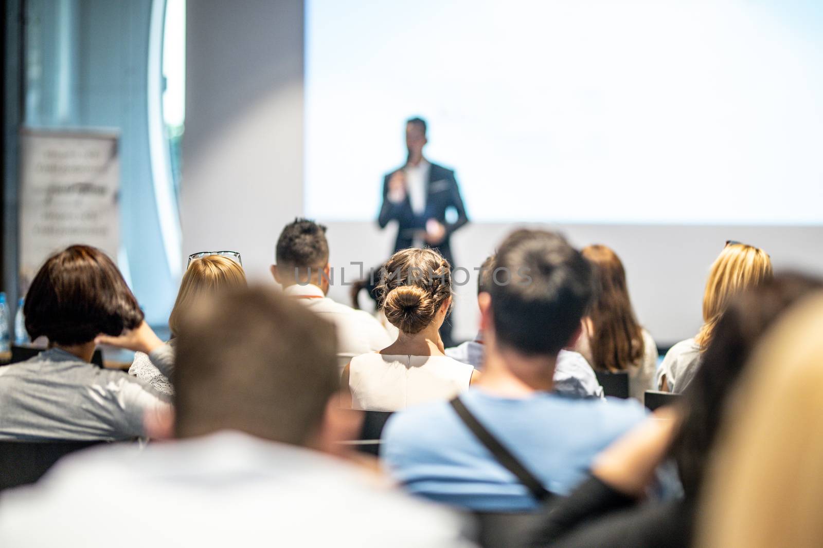 Male speaker giving a talk in conference hall at business event. Audience at the conference hall. Business and Entrepreneurship concept. Focus on unrecognizable people in audience.