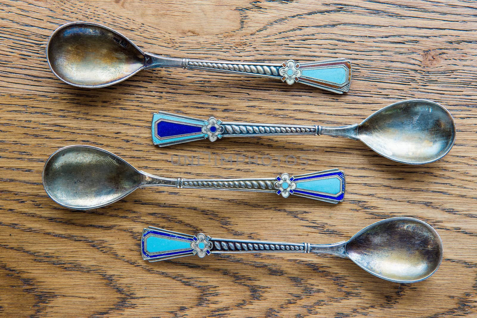 Small, antique spoons of the same size and shape lie on an oak table