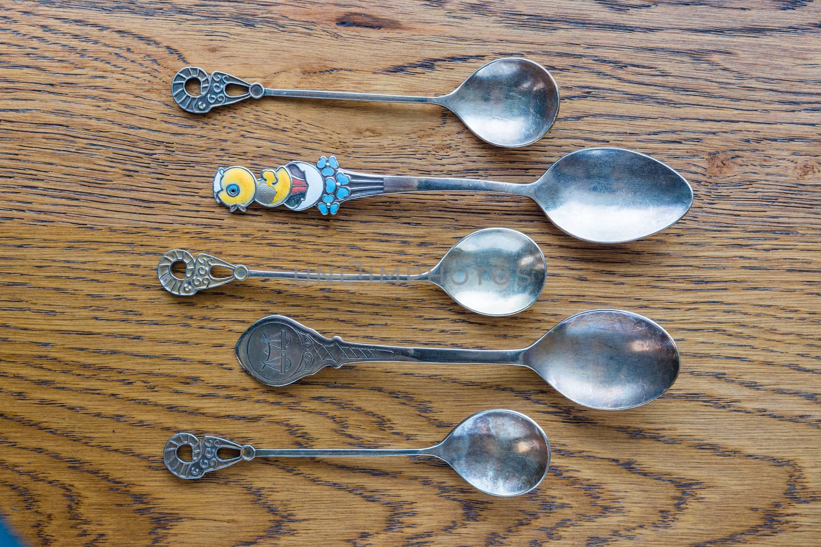 Small, antique spoons of various shapes and sizes lie on an oak table.