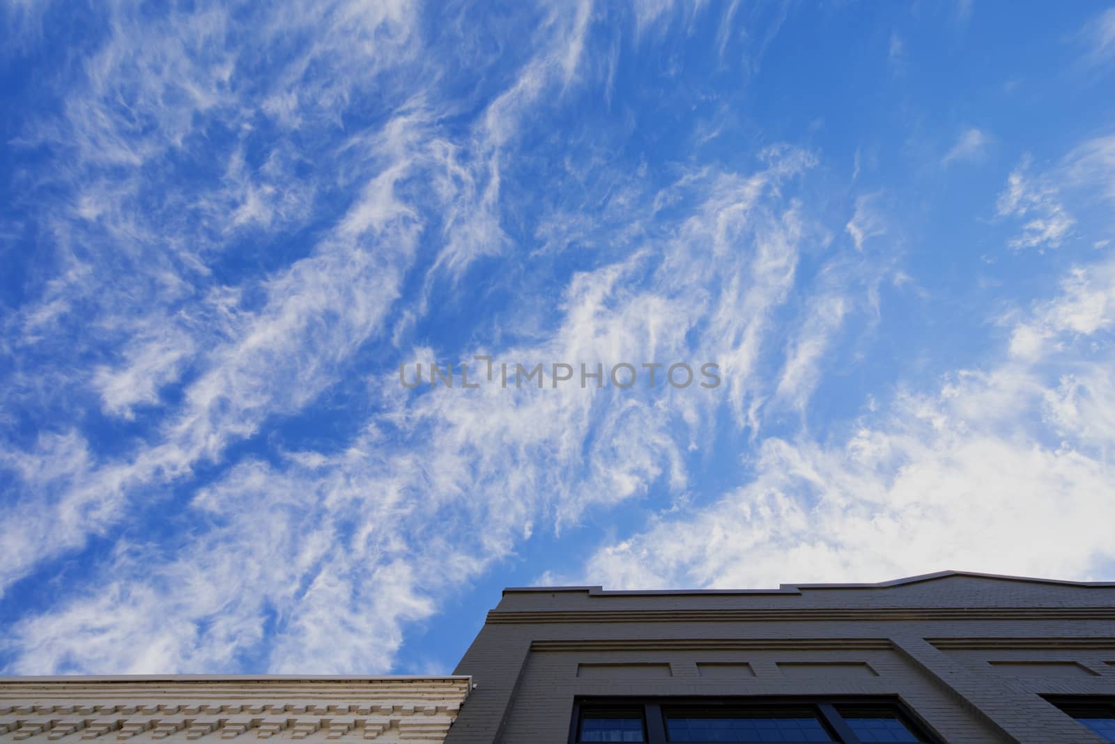 Cirrus clouds against a deep blue sky above old brick buidlings.
