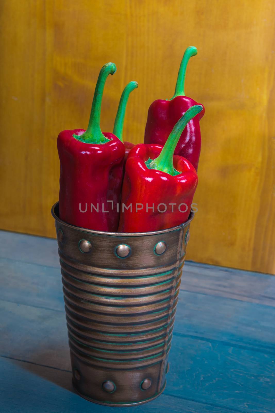 Sweet long pepper in a bucket on the blue floor against a yellow background