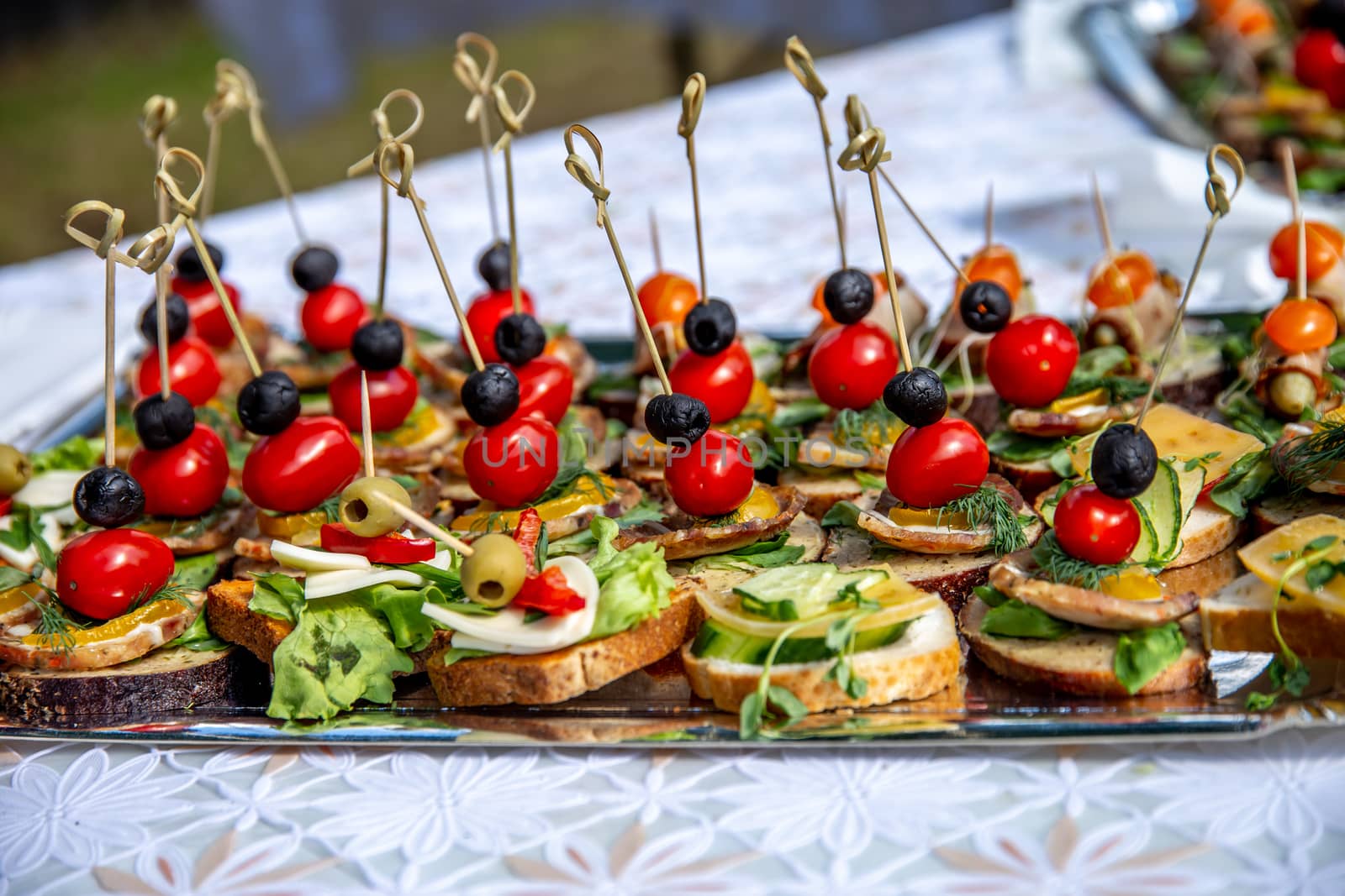 Beautifully decorated catering banquet table for wedding. Catering service buffet plate with canapes and appetizing sandwiches. Buffet catering table food. Sandwiches with meat, tomatoes, cheese, olives, cucumbers and green salads.