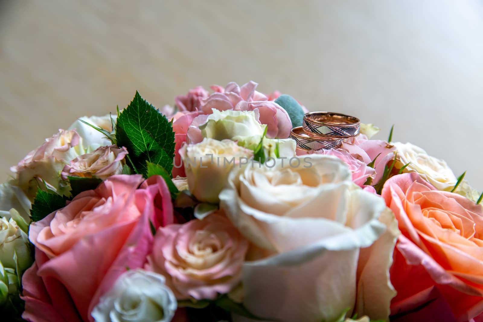 Wedding rings on the bouquet of roses. Wedding rings on bridal bouquet with colorful roses. Bouquet of bride with flowers and gold rings.

 