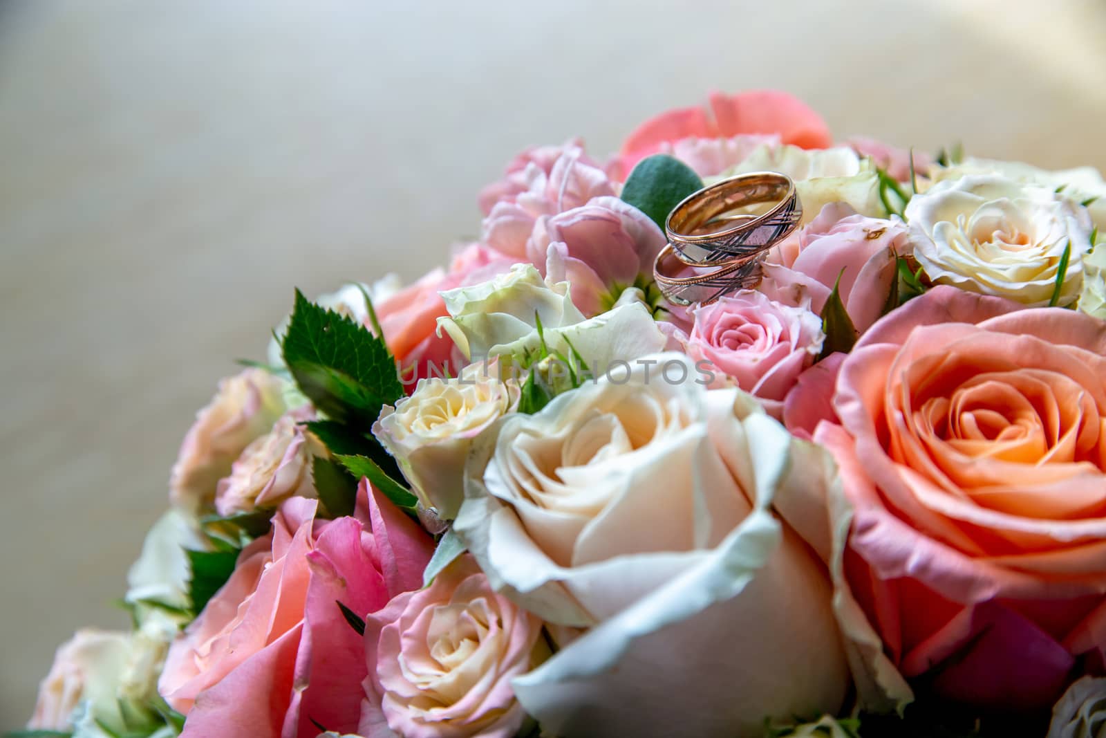 Wedding rings on the bouquet of roses. Wedding rings on bridal bouquet with colorful roses. Bouquet of bride with flowers and gold rings.

 