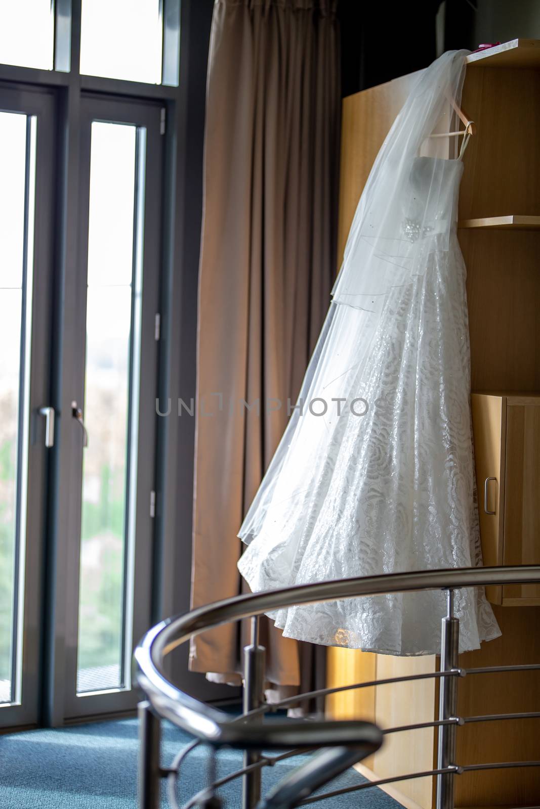 White wedding dress hanging at wooden closet. White bridal dress on the rack at the wardrobe. Wedding clothes for the bride.