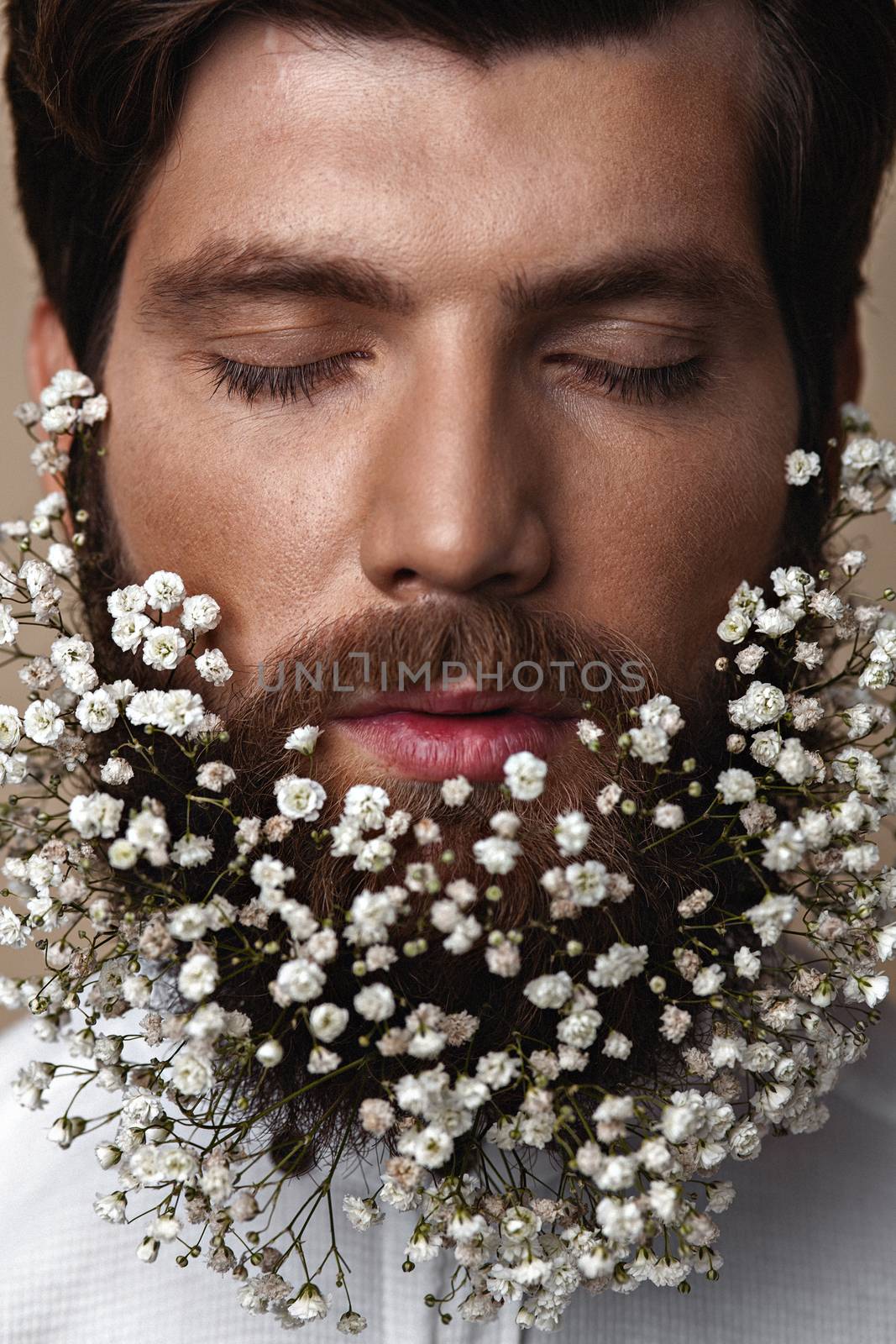 Creative Portrait of young beautiful man with a beard decorated with flowers.