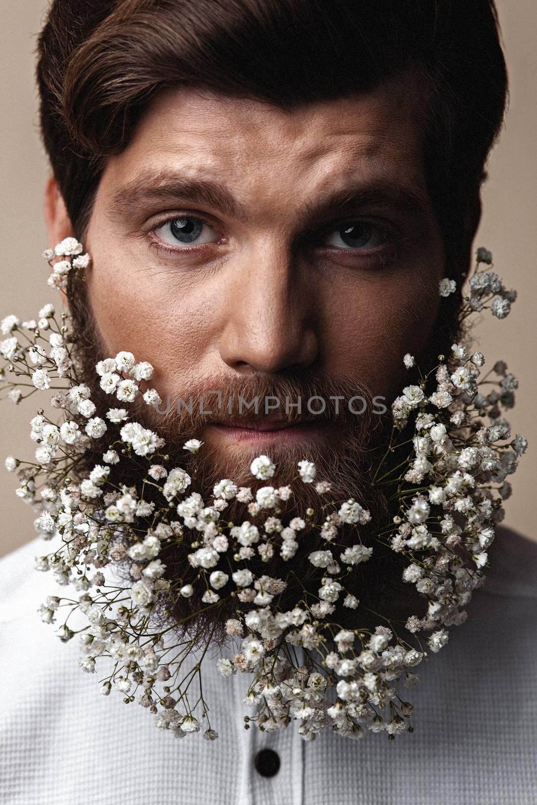 Creative Portrait of young beautiful man with a beard decorated with flowers.