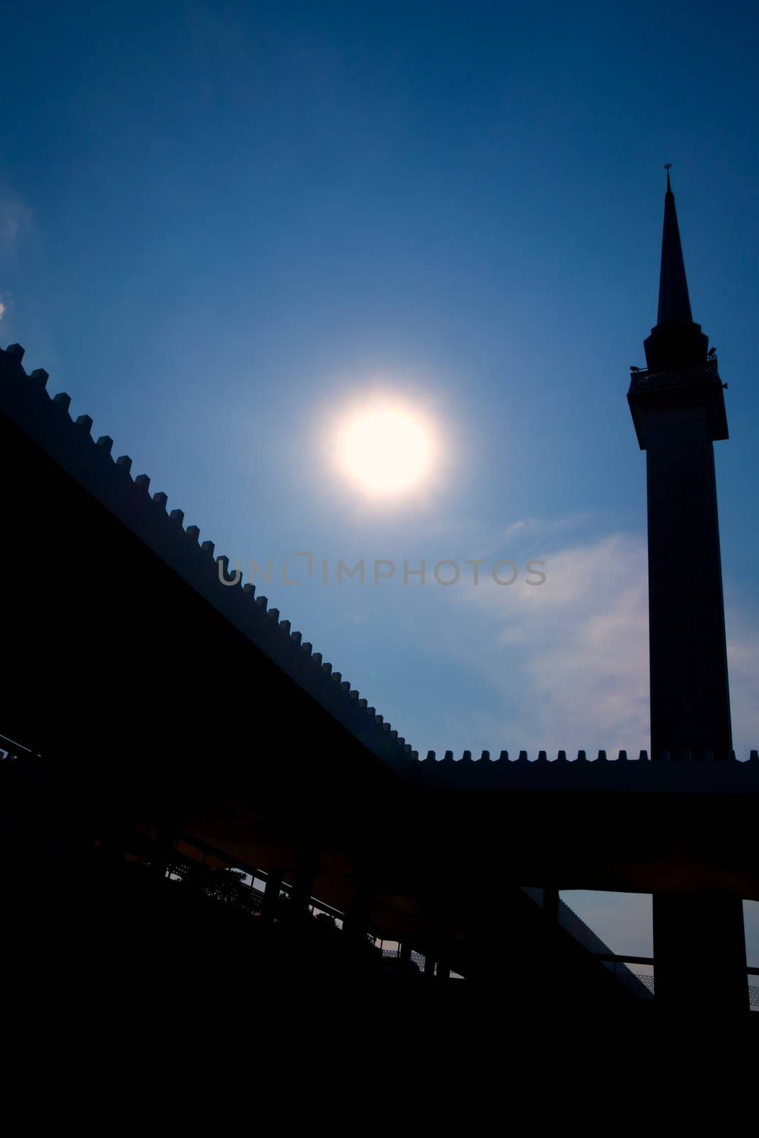 modern minaret against the sun with blue sky background and discreet cloud