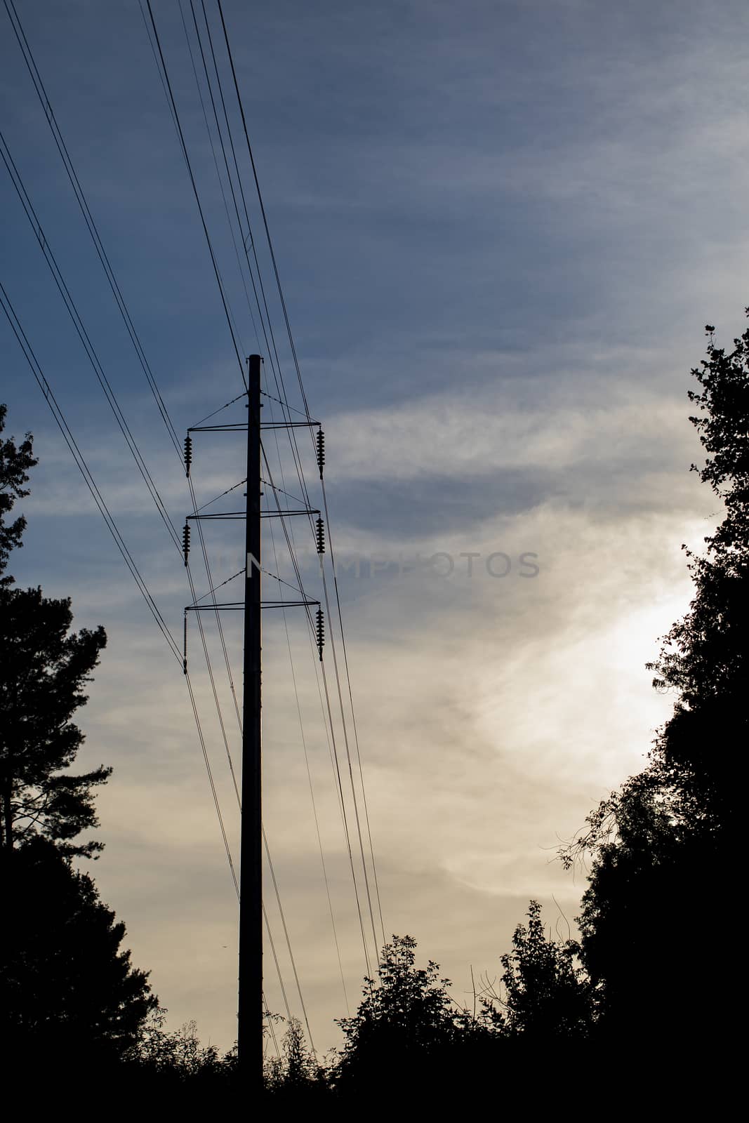Pole type high tension electrical transmission tower with lines and insulators. Tower is seen in silhouette against partly cloudy sky.